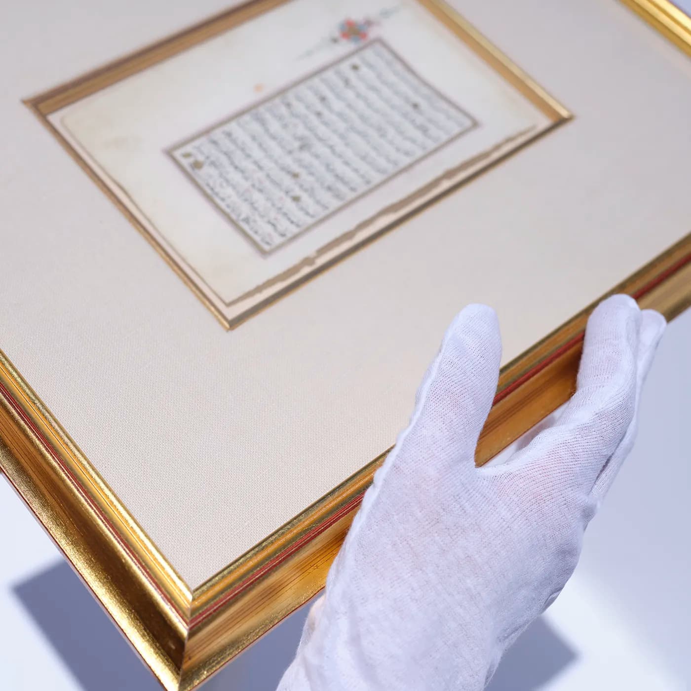 A white-gloved conservator holding a framed antique manuscript with gold-leaf border